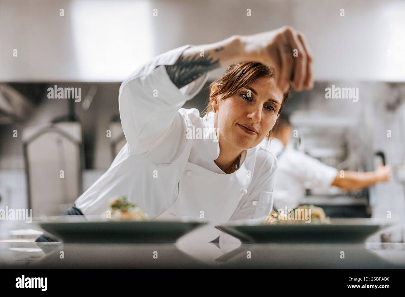 Weibliche Köchin streut Petersilie auf das Essen an der Küchentheke im Restaurant Stockfoto