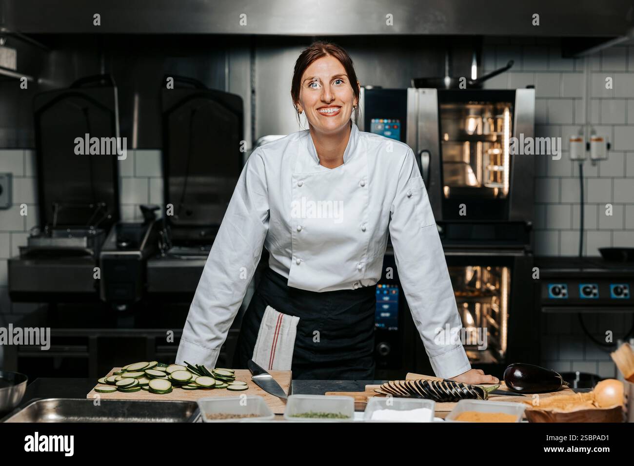 Porträt einer lächelnden Küchenchefin in weißer Uniform und in der Nähe der Theke in der Küche im Restaurant Stockfoto