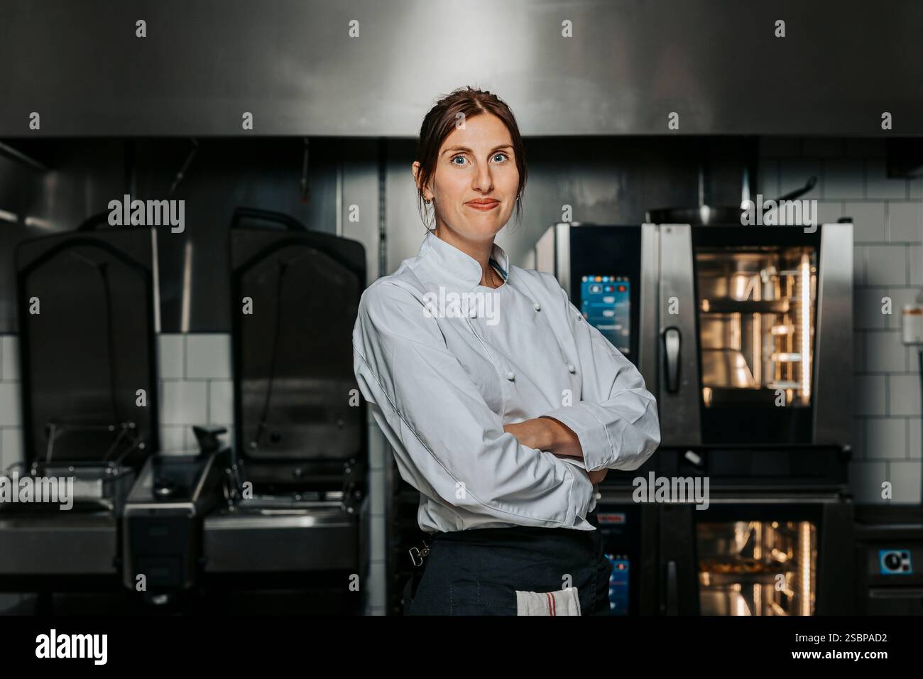 Porträt einer selbstbewussten Küchenchefin in weißer Uniform und stehend mit überkreuzten Armen in der Küche im Restaurant Stockfoto