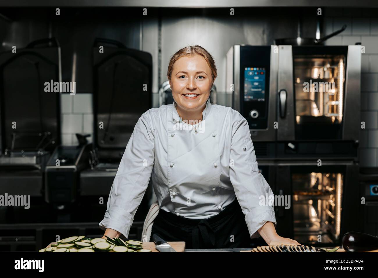 Porträt einer lächelnden jungen Küchenchefin in weißer Uniform und auf der Theke in der Küche im Restaurant Stockfoto