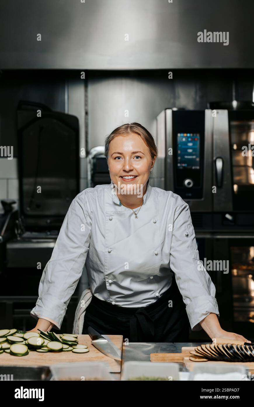 Porträt einer lächelnden Küchenchefin in weißer Uniform und auf der Theke in der Küche im Restaurant Stockfoto