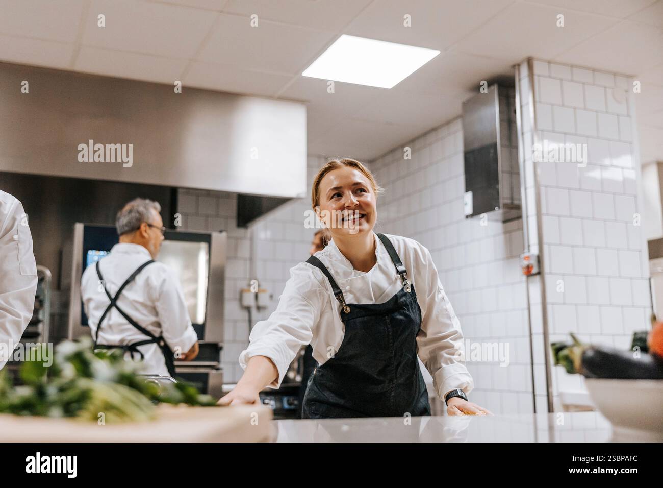 Flacher Blick auf die lächelnde Küchenchefin, die in der Küche des Restaurants in der Nähe der Theke steht Stockfoto
