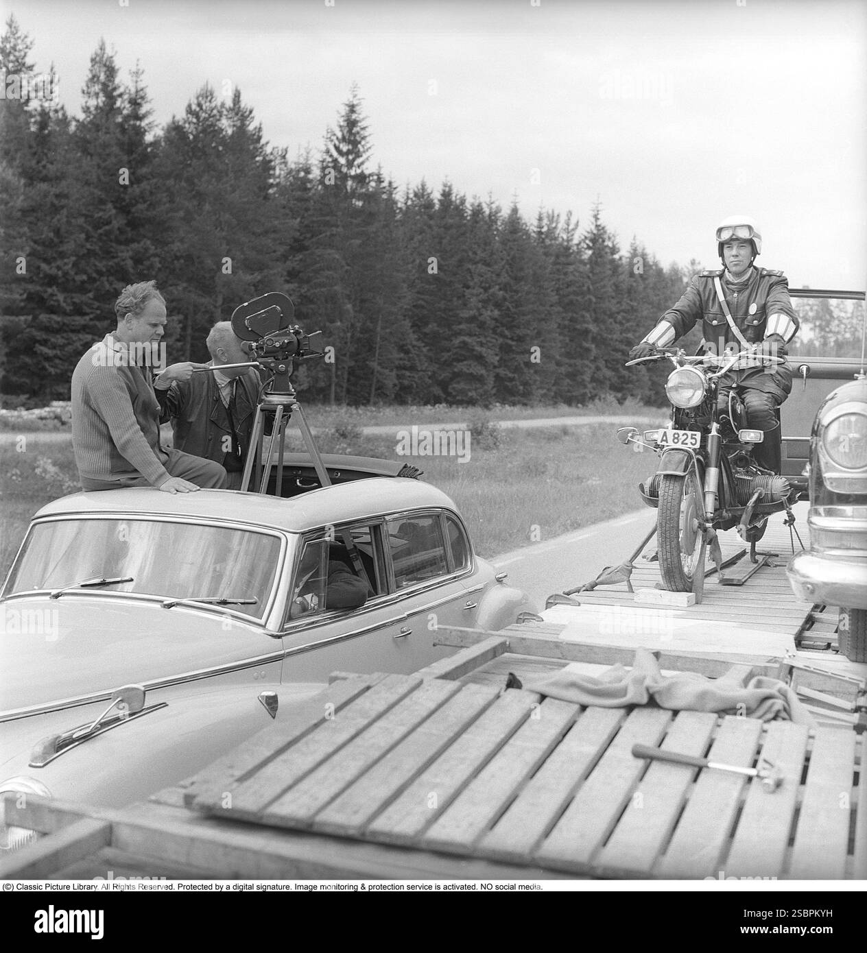 Das Gelbe Auto. Schwedischer Thriller aus dem Jahr 1963 unter der Regie von Arne Mattsson. Der Film ist einer von mehreren sogenannten Hillman-Filmen, die auf Detektivromanen des Autors Folke Mellvig basieren. Karl-Arne Holmsten spielt die Rolle des Privatdetektivs John Hillman. Das Bild zeigt Arne Mattsson und den Kameramann Bertil Wiktorsson in einem Auto, in dem die Filmkamera aus der Dachluke ragt. Daneben befindet sich ein Polizeimotorrad auf einem LKW und Claes Esphagen in der Rolle des Polizisten. Die Art, wie die Szene gedreht wurde, ließ es aussehen, als würde das Motorrad fahren. Der Film hatte seine schwedische Premiere am 29. Juli Stockfoto