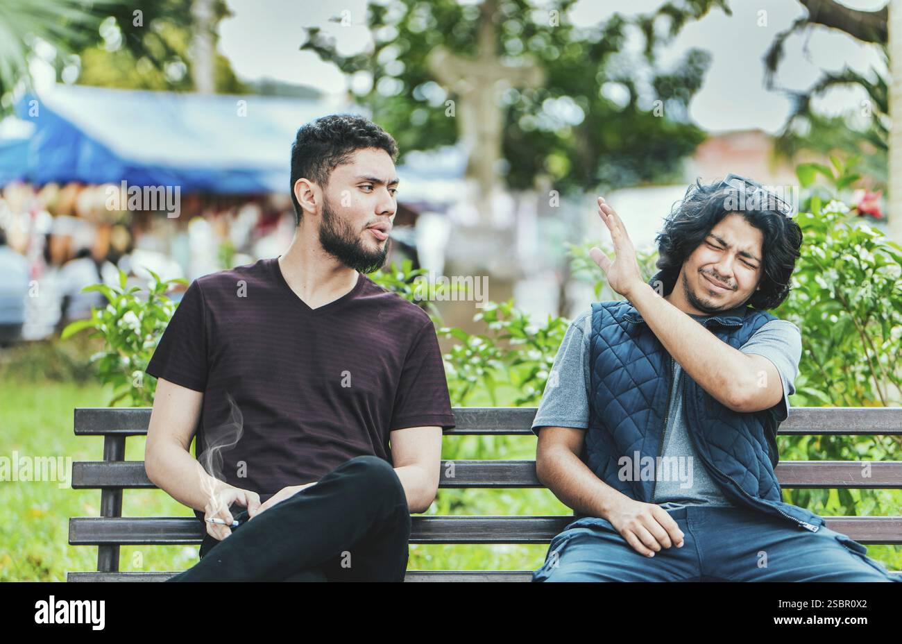 Ein Mann raucht und atmet Rauch an eine andere Person in seiner Nähe aus. Mann raucht Zigarette in der Nähe von Menschen in der Öffentlichkeit Stockfoto