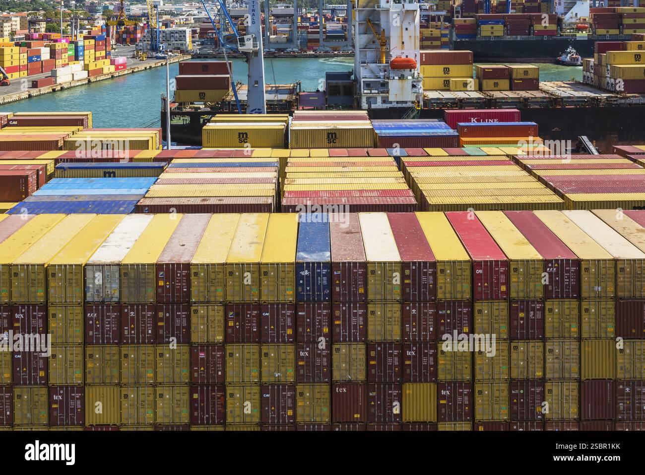 Hochwinkelansicht der gestapelten rechteckigen Metallkisten in Gelb, rötlich braun und blau am Dock im Frachthafen La Spezia, Italien, Europa Stockfoto
