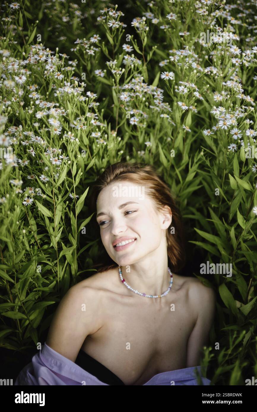 Eine Frau mit Halskette lächelt friedlich, während sie auf einem Blumenfeld liegt Stockfoto