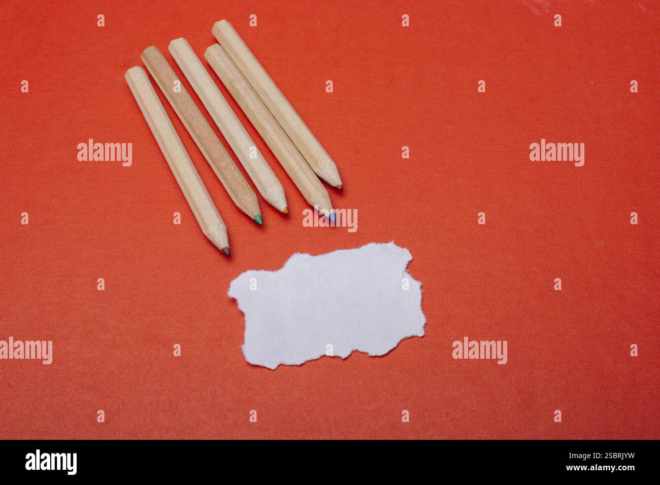 Buntstifte auf rotem Hintergrund und zerrissenes Papier Stockfoto