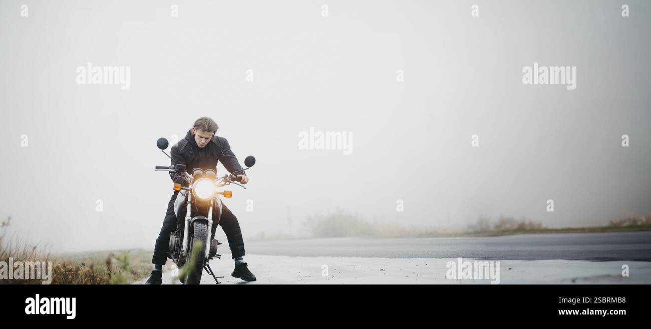 Ein Fahrer lehnt sich über ein Motorrad mit eingeschalteten Scheinwerfern in nebeliger Umgebung Stockfoto
