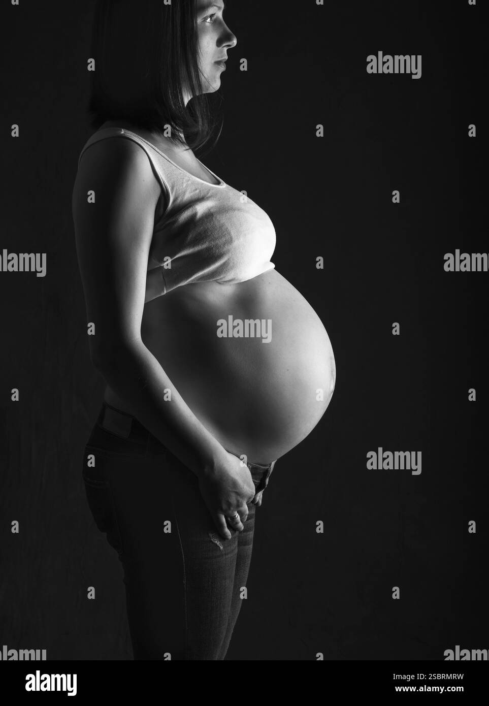 Schwangere Frau, werdende Mutter auf schwarzem Hintergrund, Nahaufnahme des schwangeren Bauches, Aktivität während der Schwangerschaft, Monoschrome-Shooting Stockfoto