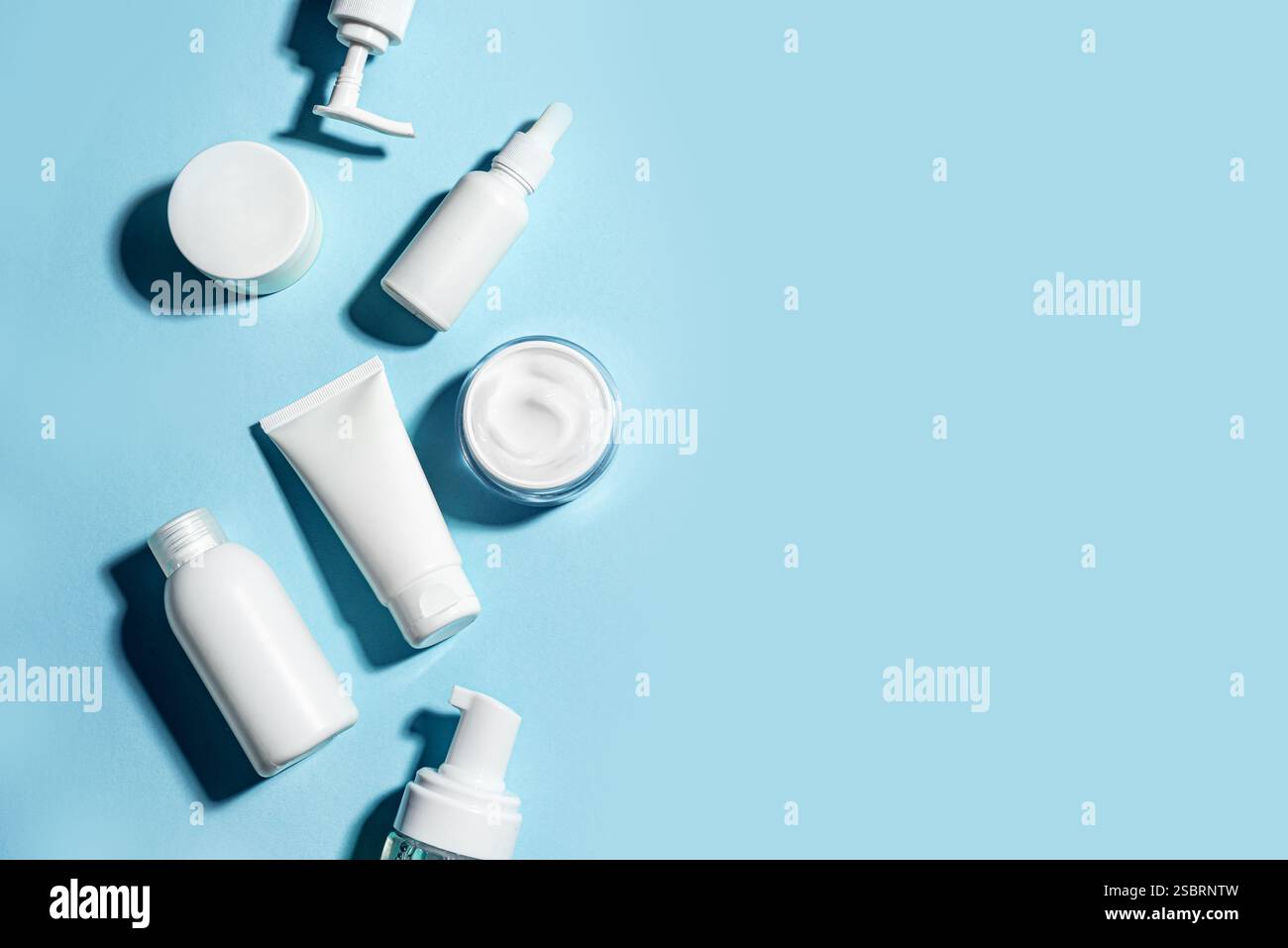 Verschiedene weiße Kosmetikbehälter auf blauem Hintergrund, kreatives Layout, Kopierraum. Leere Kosmetikprodukte für das Gesicht, Reisehygiene-Set, Hautpflege minimal Stockfoto
