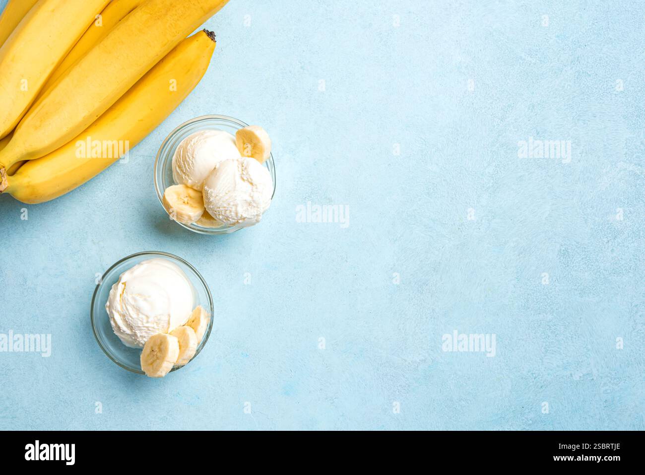 Eislöffel und Bananenscheiben in Schüsseln auf blauem Hintergrund, Draufsicht, Kopierraum. Gesundes rohes veganes Bananeneis (Nicecream), hausgemachte Bio Stockfoto