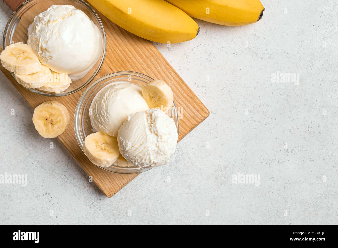 Eiskugeln und Bananenscheiben in Schüsseln auf weißem Tisch, Blick von oben, Kopierraum. Gesundes rohes veganes Bananeneis (Nicecream), hausgemachte Bio-des Stockfoto