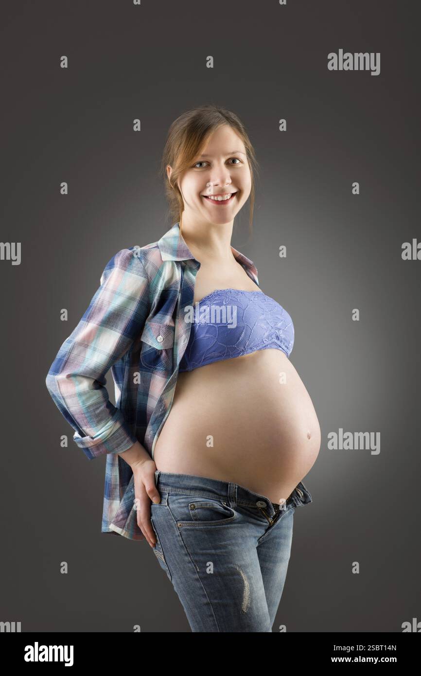 Glückliche junge schwangere Frau auf grauem Hintergrund Stockfoto