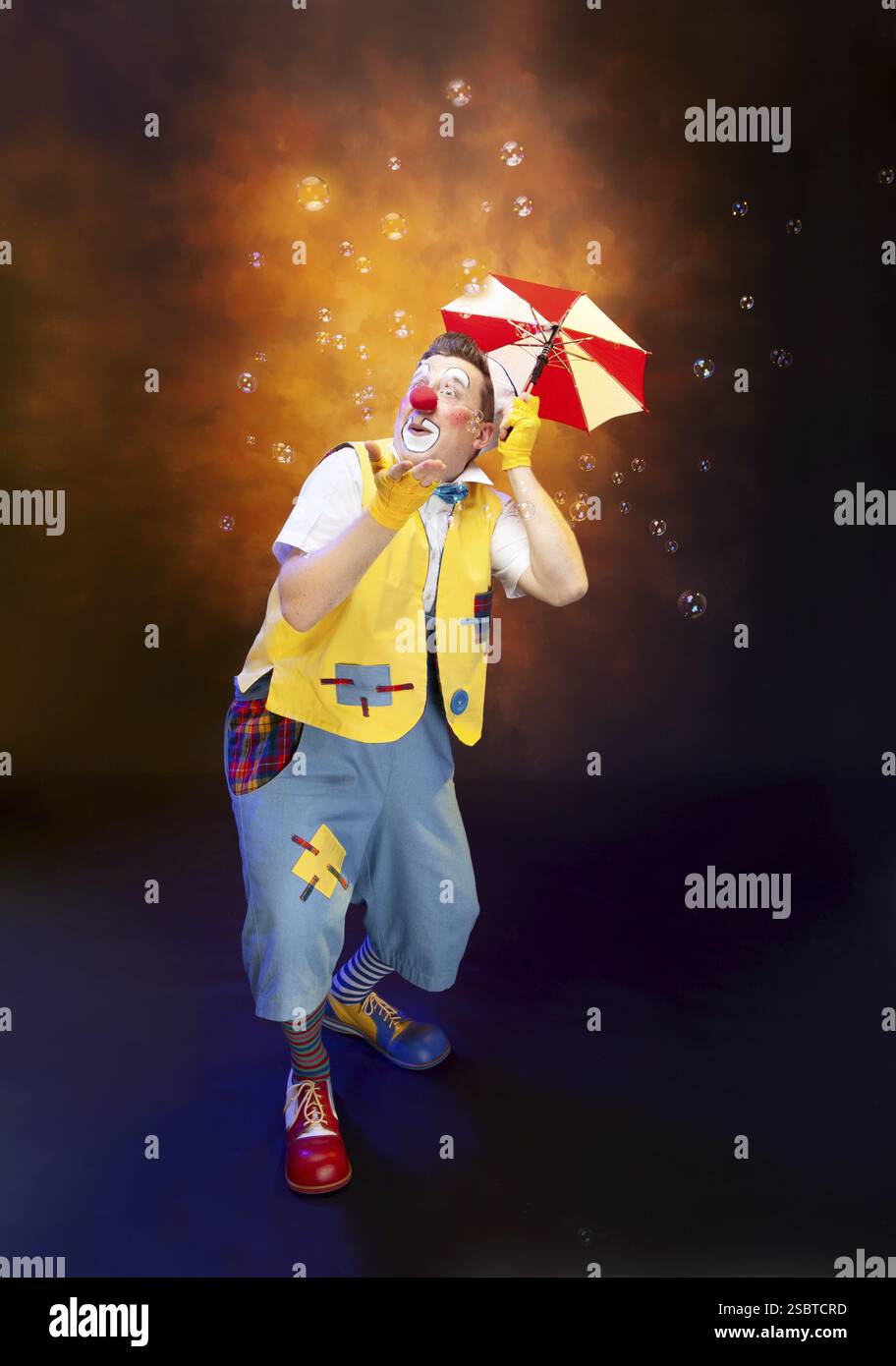 Ein lustiger Clown mit lächelndem, fröhlichem Ausdruck, auf farbigem Hintergrund Stockfoto