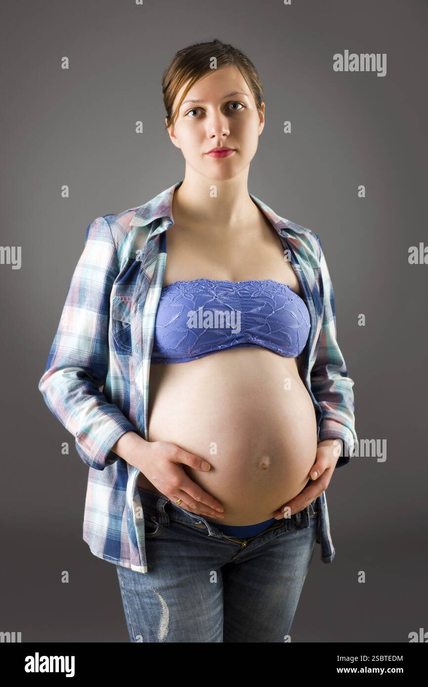Schwangere Frau streichelt ihren Bauch, über grauem Hintergrund Stockfoto