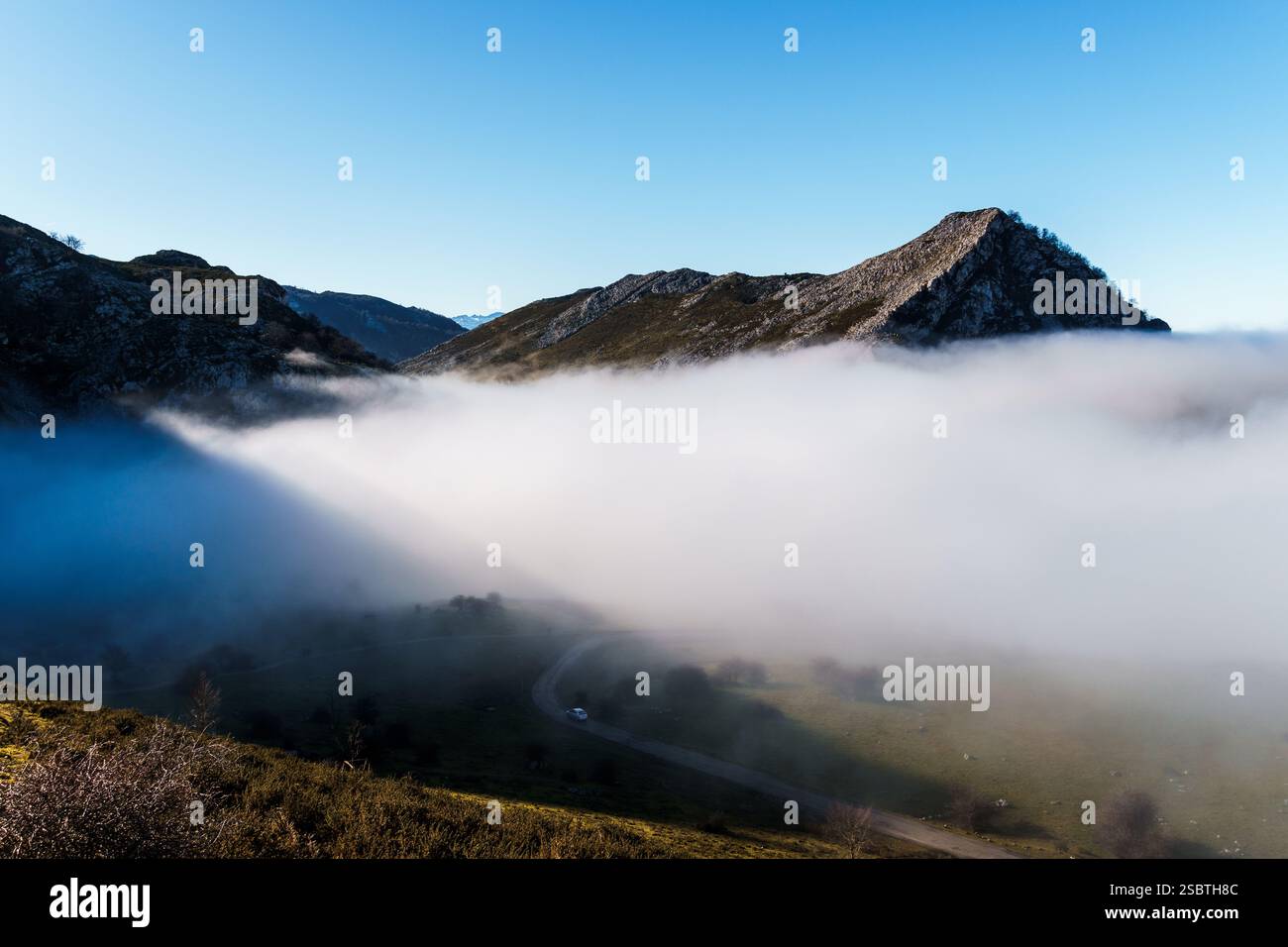 Misty Mountain Valley Road Scene, eine gewundene Straße schlängelt sich durch den Talboden mit Bergen, die auf beiden Seiten aufsteigen, teilweise von einem dicken L verdeckt Stockfoto