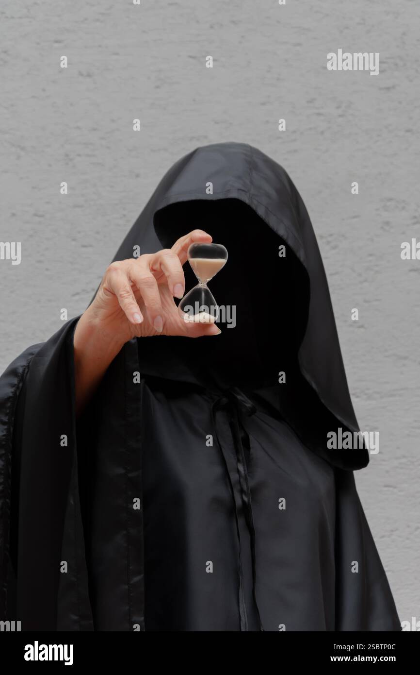 Der unbekannte Mann im schwarzen Mantel weist auf die Sanduhr als Symbol der Zeit hin Stockfoto