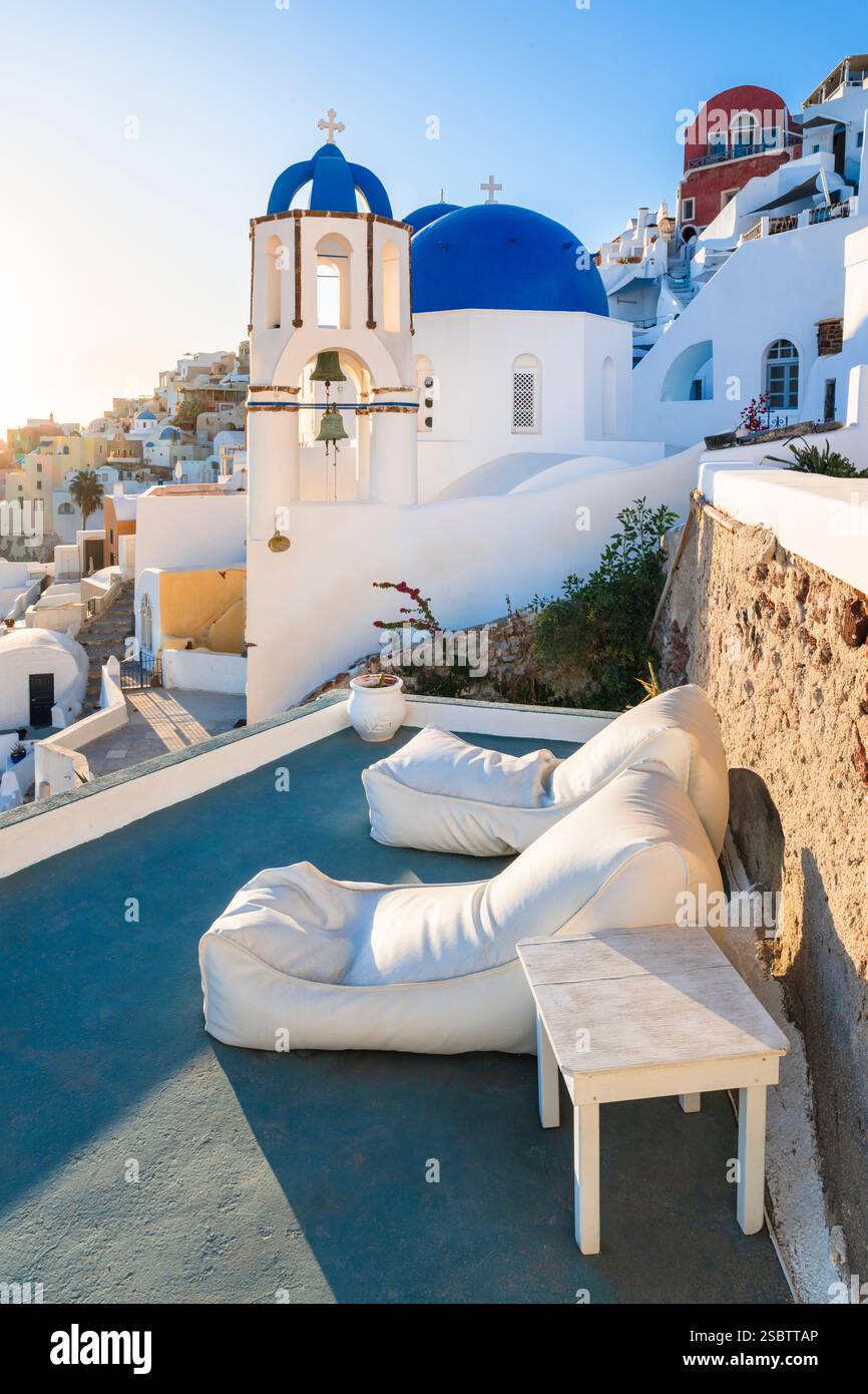 Zwei Sonnenliegen in der Abendsonne vor der Kirche St. Spyridon mit den blauen Kuppeln in Oia, Kykladen, Griechenland Stockfoto
