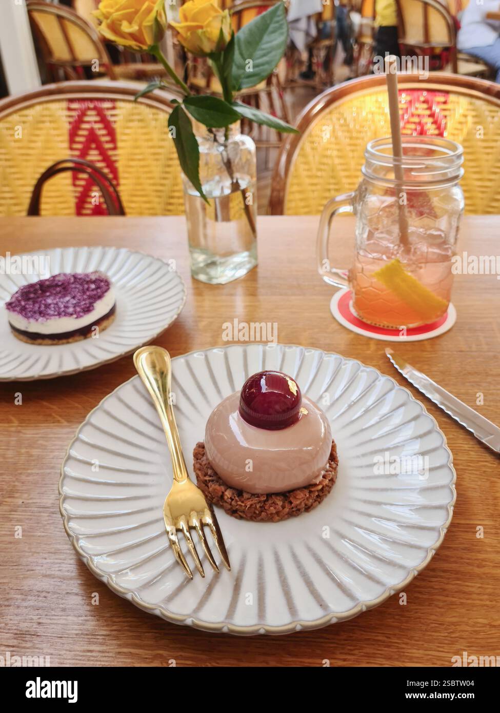Ein Beeren-Mousse-Dessert mit einem Hochglanzbelag sitzt auf einem strukturierten Teller mit einer goldenen Gabel in einem gemütlichen Café Stockfoto
