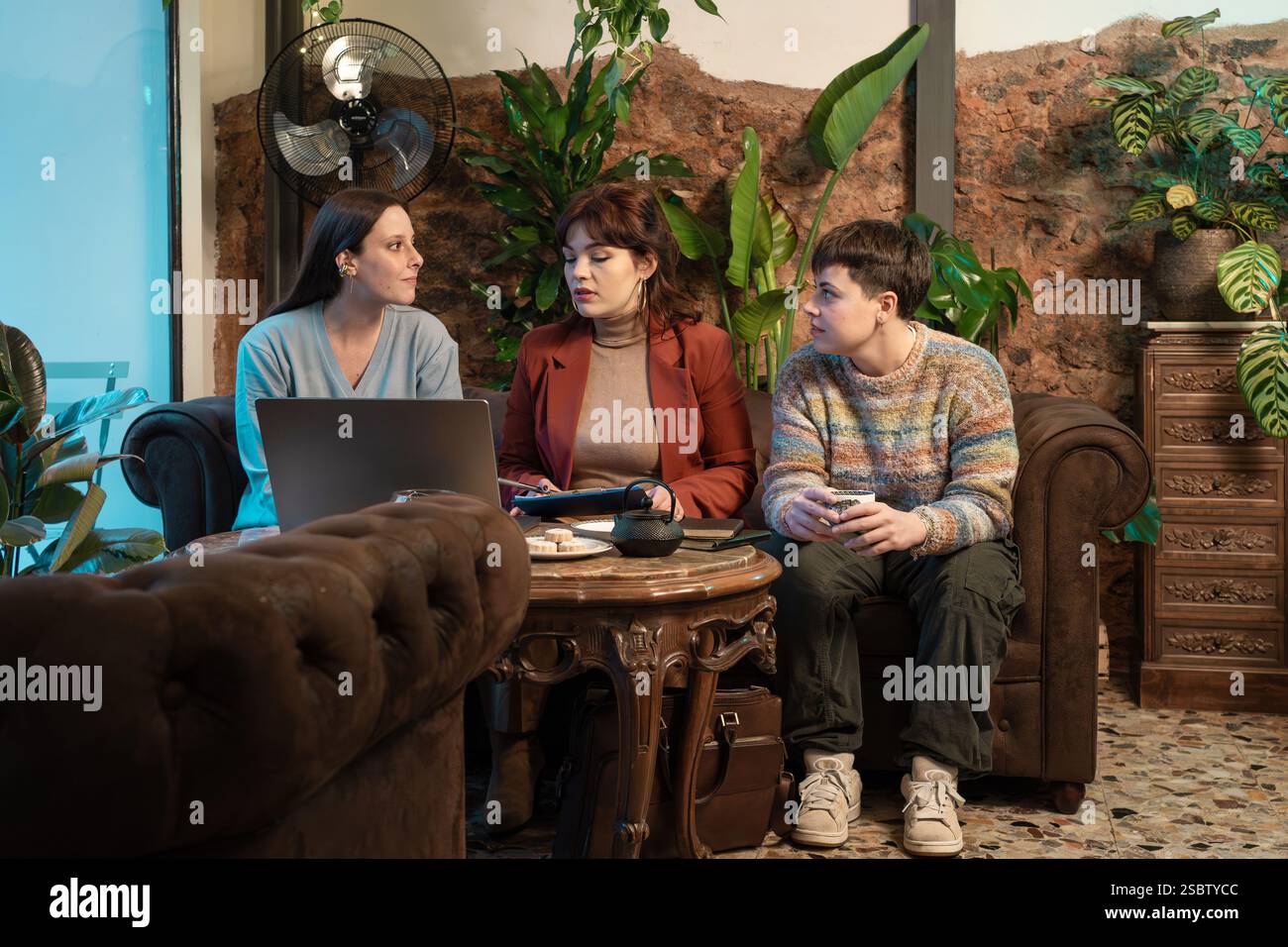 Eine vielfältige Gruppe von Frauen und einer nicht binären Person, die in einem gemütlichen Café an einem Geschäftsgespräch teilnahm, an einem Laptop arbeitete und in einer Zusammenarbeit Notizen machte Stockfoto