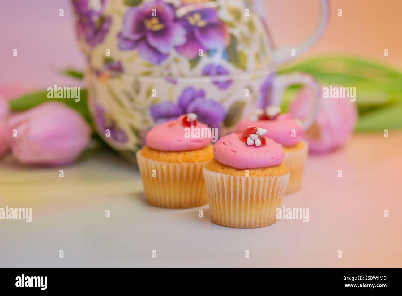 Teekanne mit Blumenmuster, Mini-Cupcakes und Tulpen für Oster- und Nachmittagstee; Konzept für Teestation, festliche Feiern, Geburtstage und Muttertag. Stockfoto