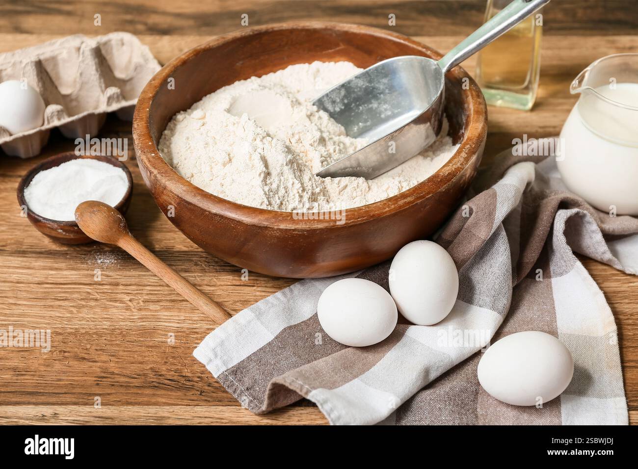 Frische Eier, eine Schüssel Mehl, Öl, Backpulver und Milch auf Holztisch Stockfoto