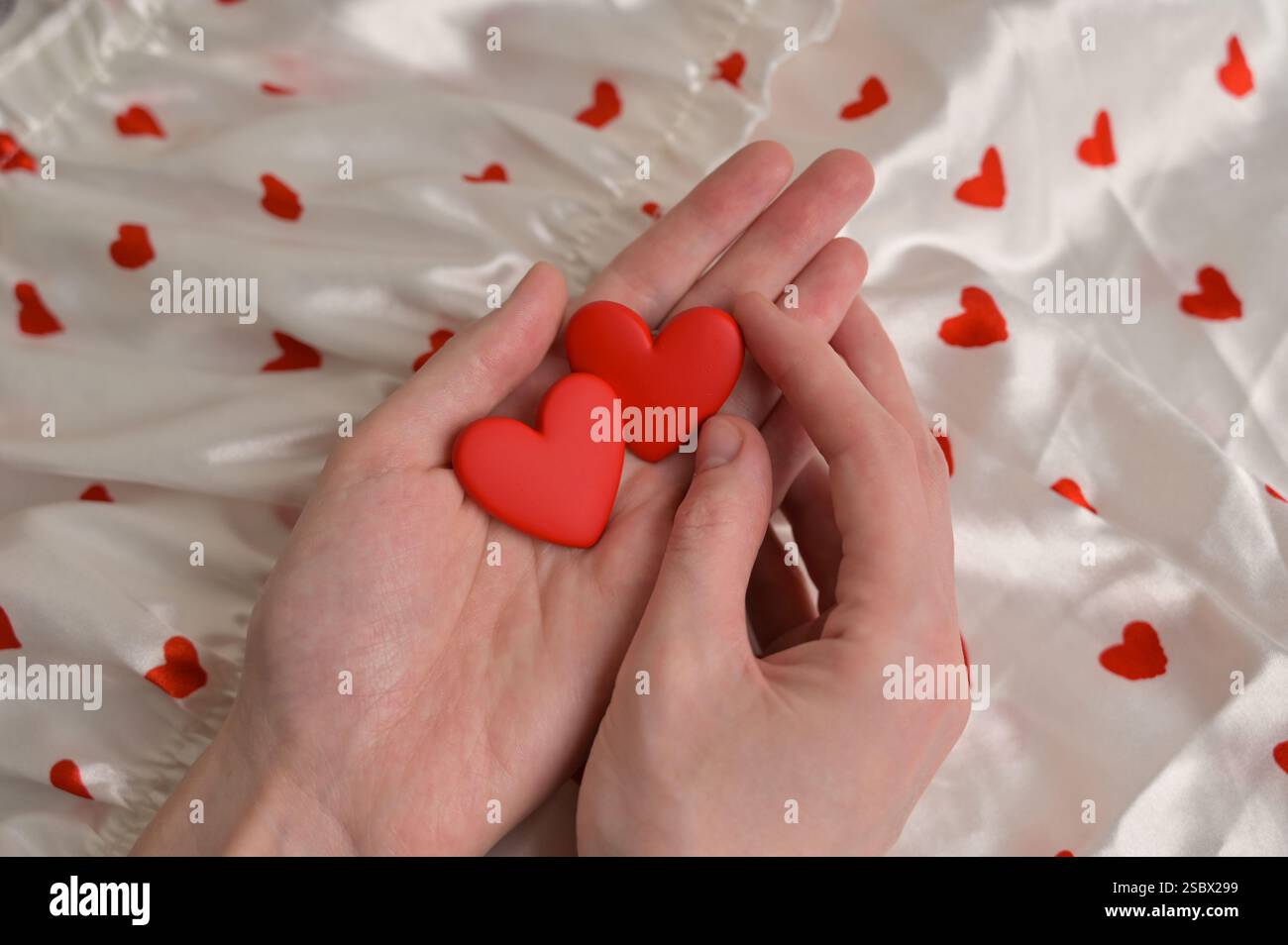 Frau, die ein paar rote Ohrringe in der Hand hält. Weißes Tuch mit herzförmigem Hintergrund. Vorbereitung auf den Valentinstag Stockfoto