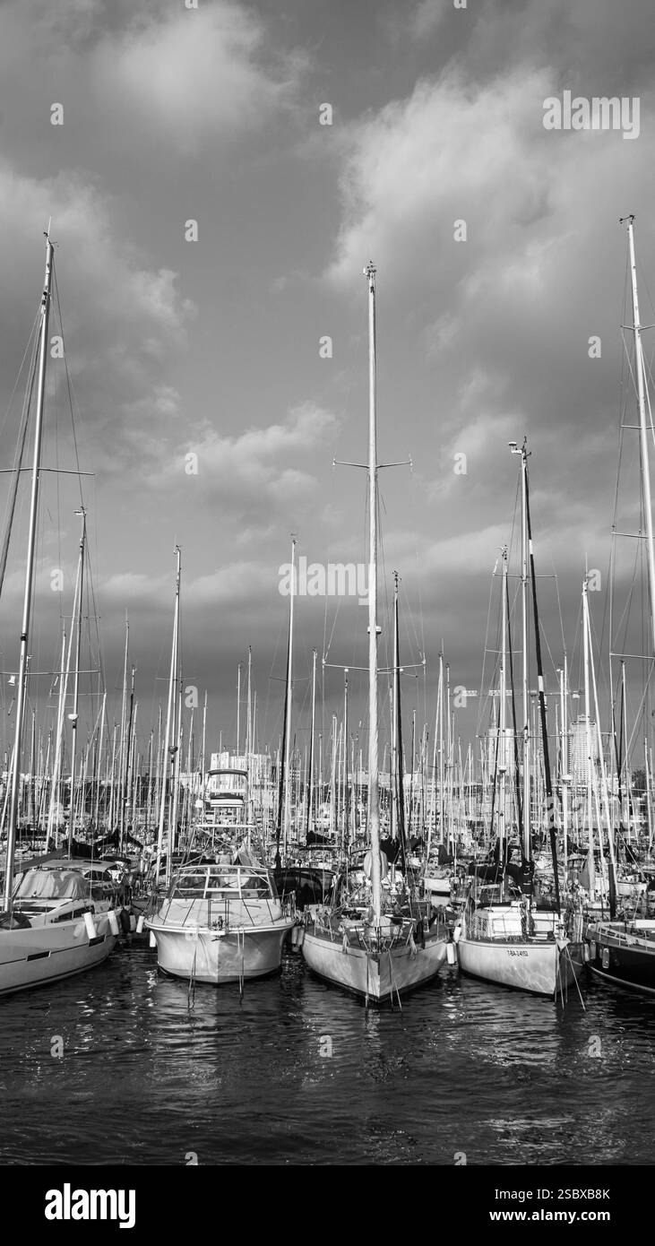 Vertikales Schwarzweiß-Foto von Segelbooten, die im sonnigen Hafen von Port Vell, Barcelona, Spanien, verankert sind Stockfoto