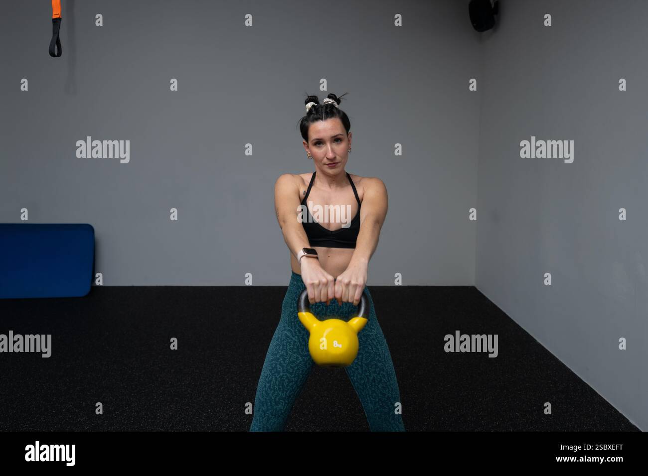 Starke weibliche Athletin, die während des Cross-Trainings im Fitness-Center gelbe Kettlebell hebt und Stärke und Entschlossenheit zeigt Stockfoto