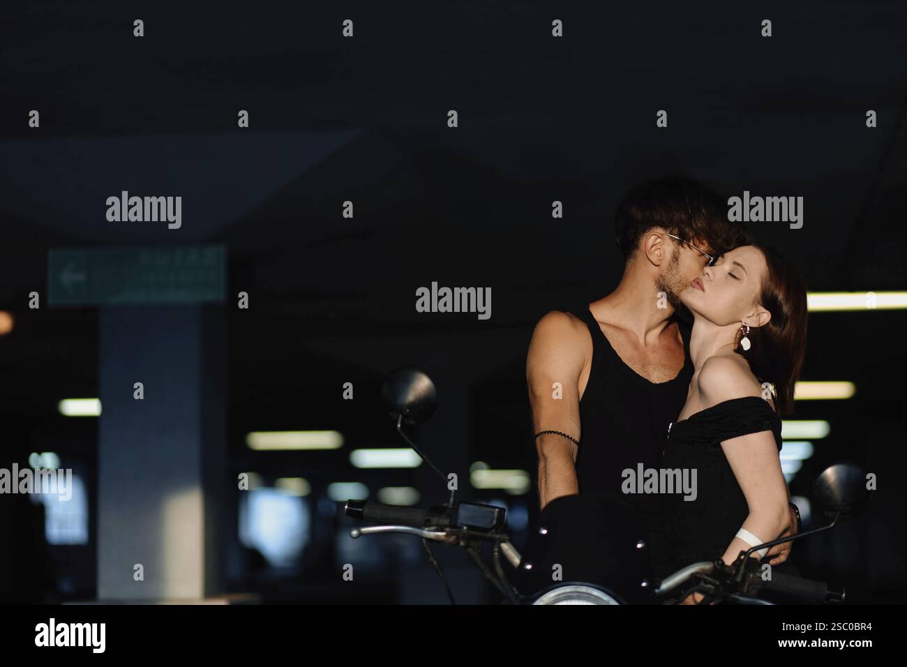 Ein Paar, das sich in einer schwach beleuchteten urbanen Umgebung intim auf einem Motorrad umgibt Stockfoto