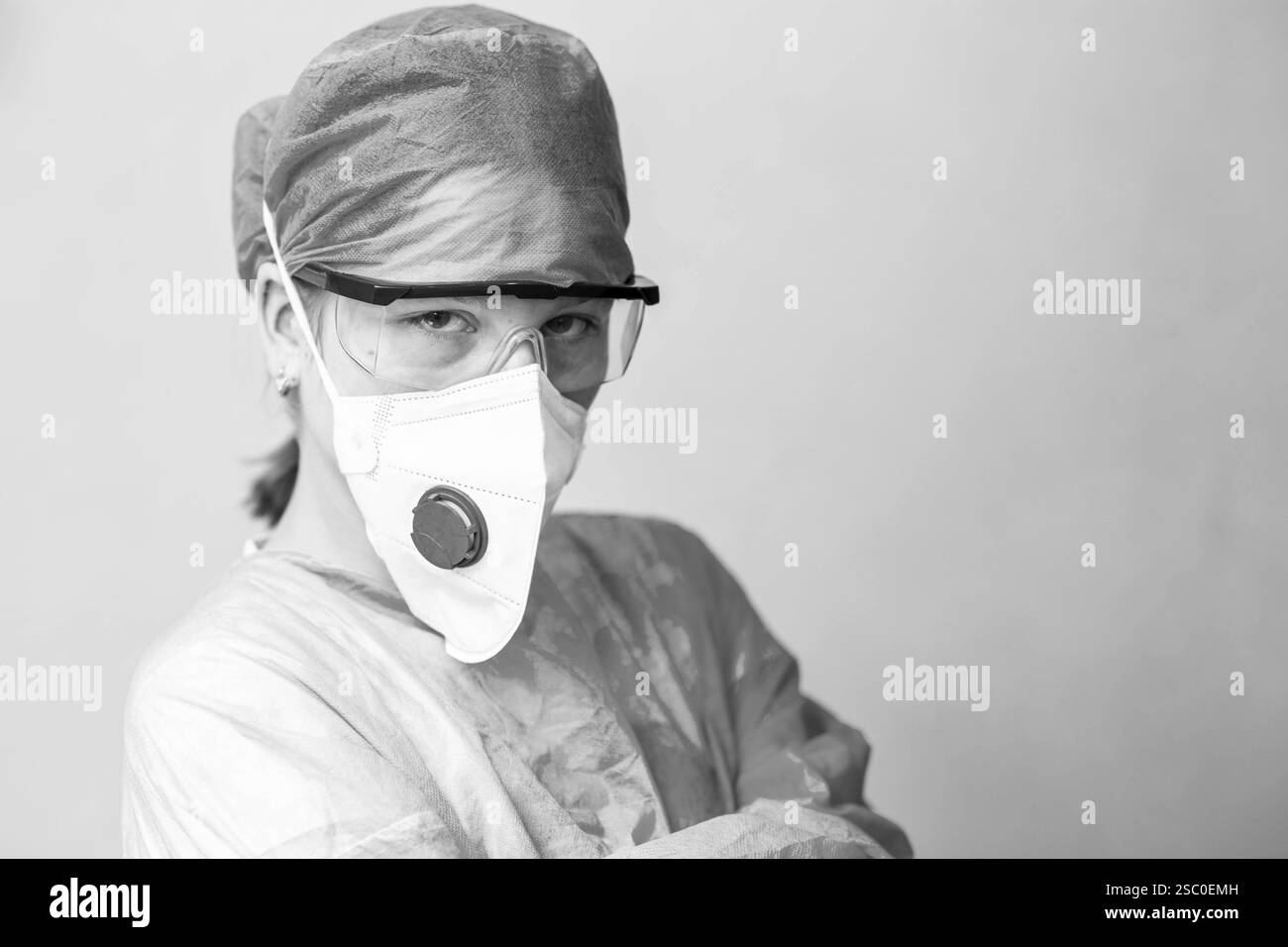 Schwarz-weiß-Bild eines Pflegepersonals in einer N95-Maske, mit einem Kreuz bewaffnet, mit einem intensiven Ausdruck Stockfoto
