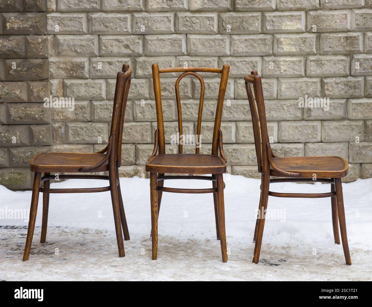 Klassische Bugholzstühle ruhen in einer verschneiten Landschaft an einer Backsteinmauer und erinnern an Vintage-Charme und ruhige Nostalgie. Stockfoto