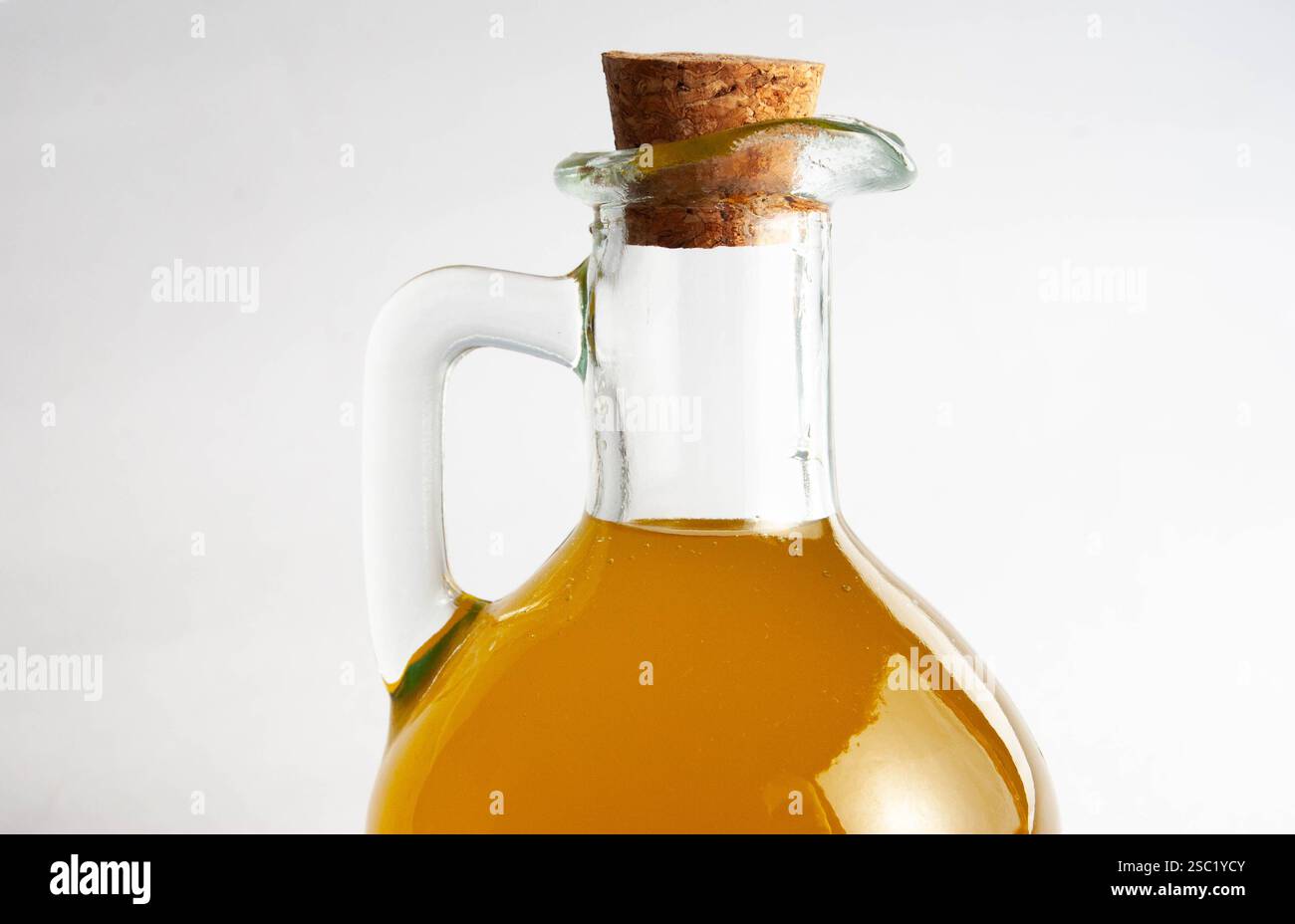 Eine wunderschön gefertigte Glasflasche gefüllt mit goldenem extra nativem Olivenöl, versiegelt mit einem natürlichen Korkdeckel, platziert auf einem sauberen weißen Hintergrund. Stockfoto