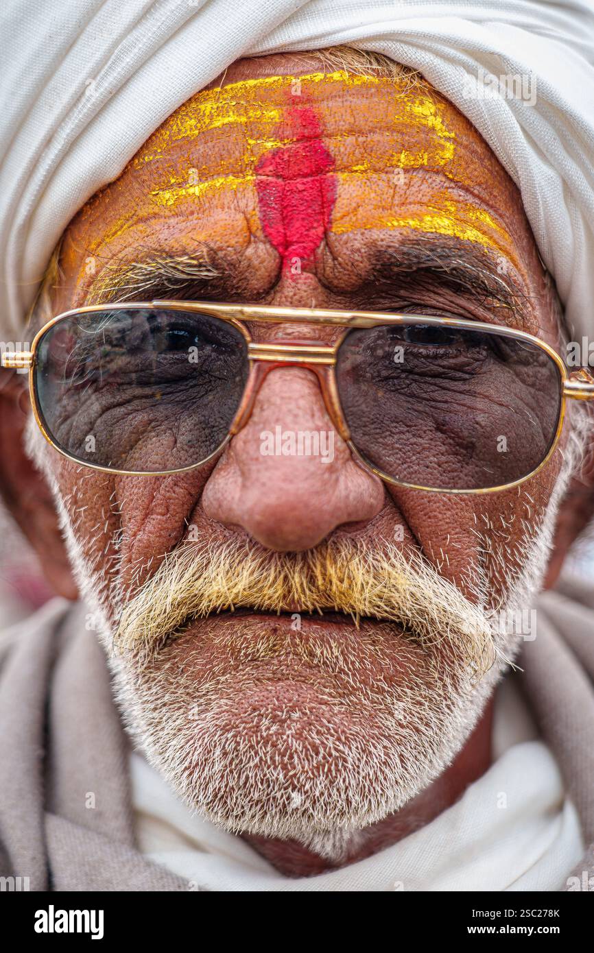 13. Januar 2025, Prayagraj, uttar Pradesh, Indien. Nahaufnahme eines alten Mannes, der eine Sonnenbrille trägt, mit einem Safran tilak, der Weisheit ausstrahlt. Stockfoto