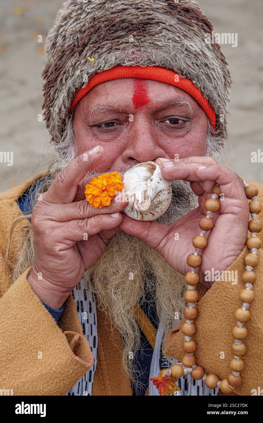 Ein Sadhu, der einen Sankha hält, geht nach seinem heiligen Bad in Richtung Sangam, der Muschel, die den Ruf zum spirituellen Erwachen und göttlichen Segen symbolisiert. Stockfoto