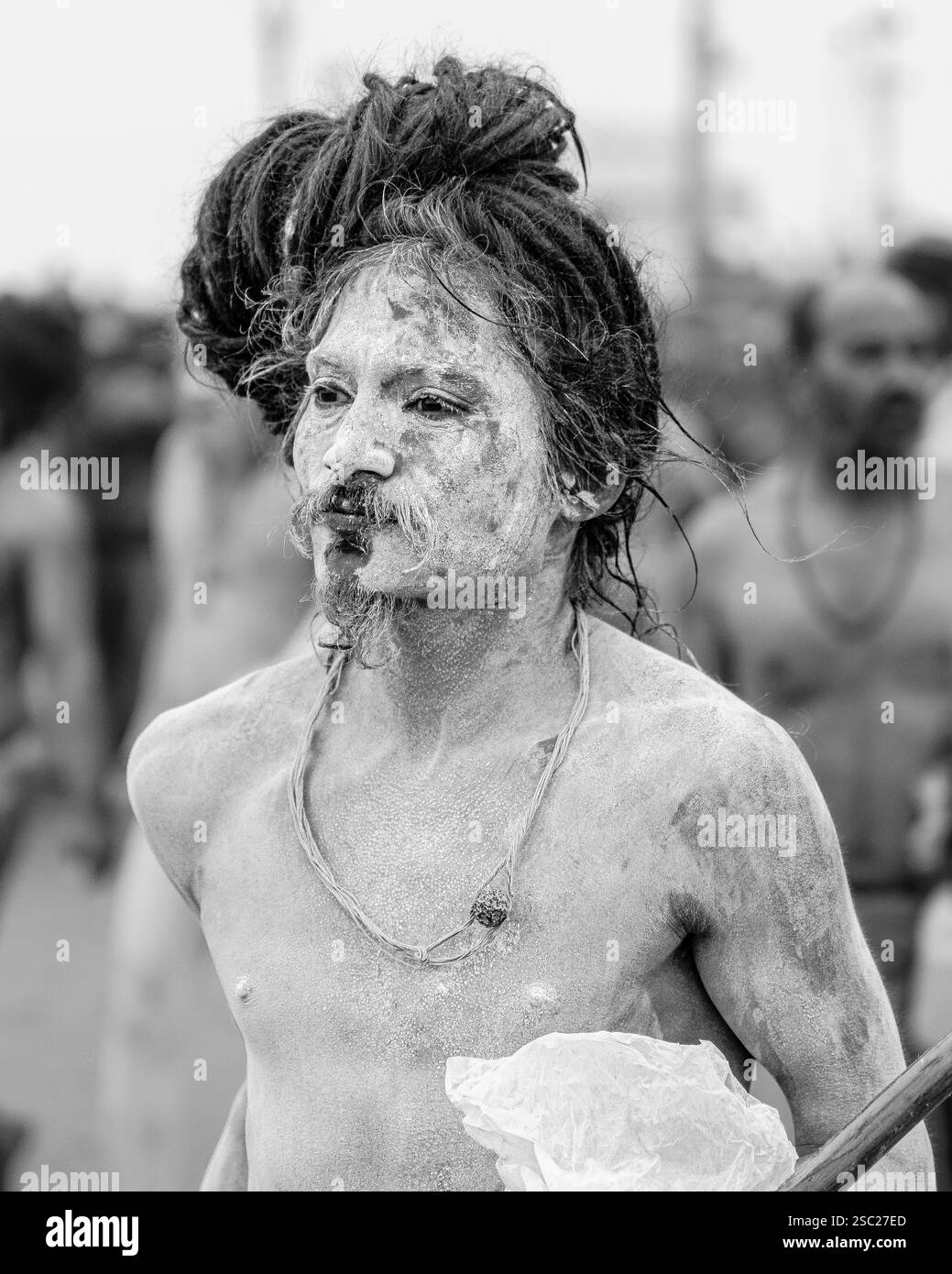Ein schlanker Naga Sadhu, sein langer jata, der mit dem heiligen Wasser fließt, steht mit heiterer Kraft nach dem heiligen Bad und verkörpert Hingabe und Askese. Stockfoto