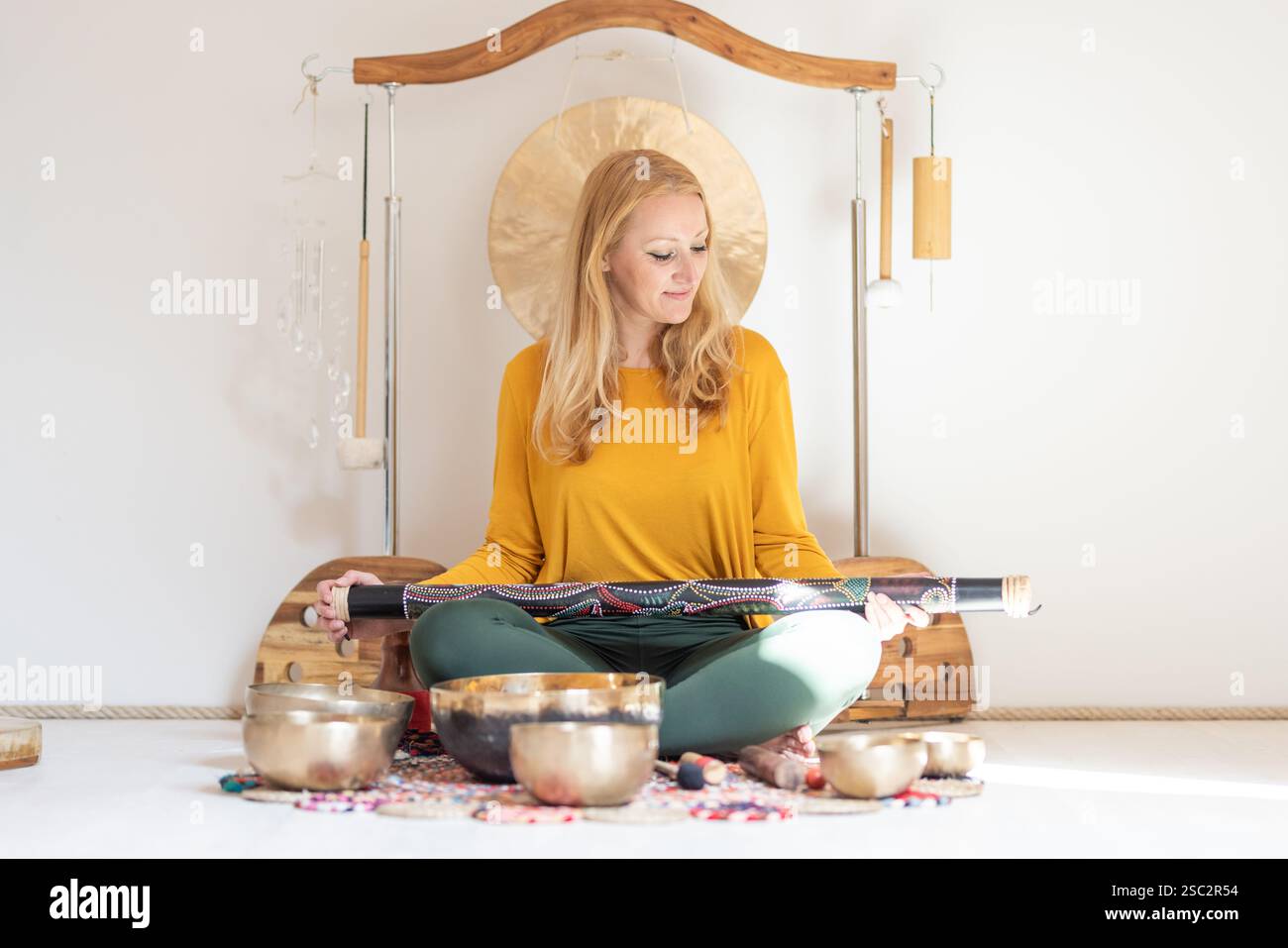 Junge fröhliche Frau, die Musiktherapiesitzungen mit traditionellen Instrumenten durchführt. Klangmeditation, Körperheilung. Sieben Chakren. Gesundheitswesen Freizeit Stockfoto