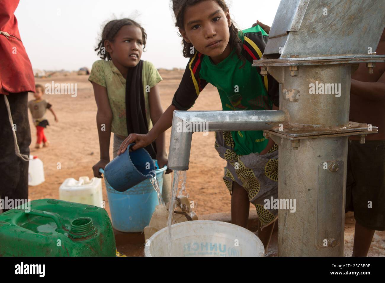 Mentao Camp for malian Refugees, bei Gibo, im Norden Burkina Fasos Mai 2012: Kinder ziehen Wasser aus einer Camp-Handpumpe. . Die Flüchtlinge, meist Tuaregs, sind allein in Burkina Faso heute mehr als 60.000 Menschen und kommen nach dem politischen Chaos, das am 22. März 2012 durch einen Staatsstreich der malischen Junioren entstanden ist, täglich in die Lager. Foto von Mike Goldwater Stockfoto