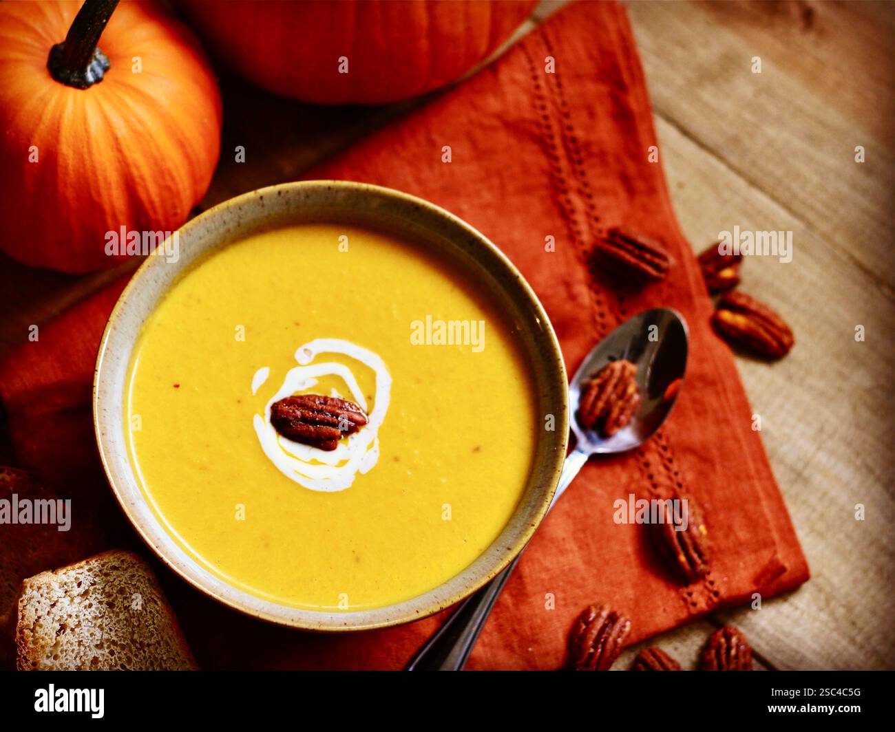 Cremige Kürbissuppe mit Pekannüssen und Creme, auf rustikalem Holz mit Herbstdekor Stockfoto