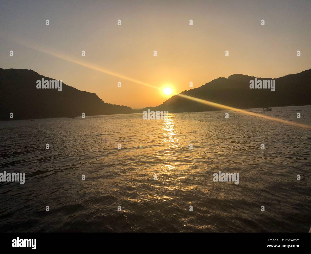 Die hellgelbe Sonne untergeht hinter einem Berg, während sie sich auf dem Meer reflektiert - Smartphone-aufgenommenes Stockfoto