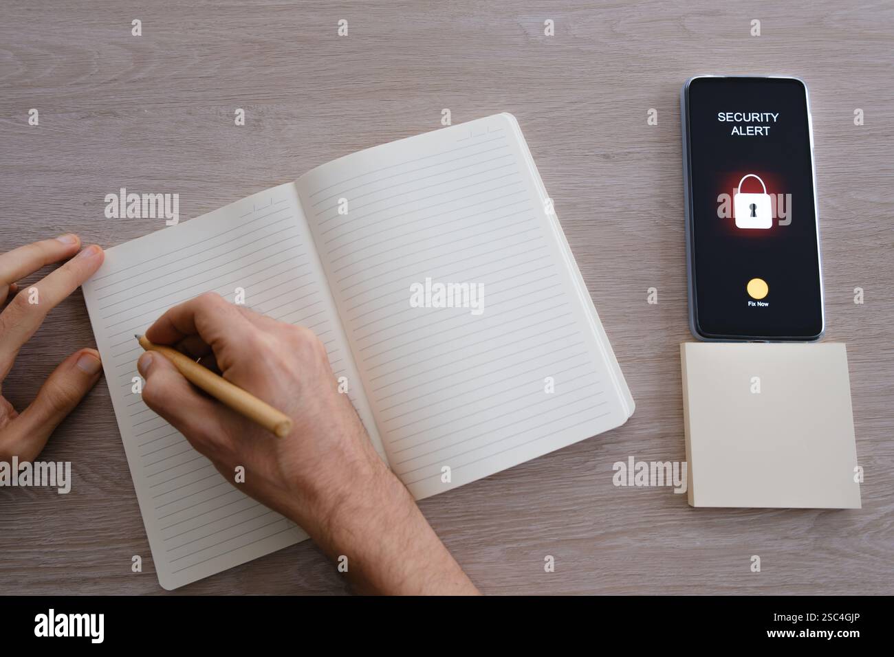 Person, die in Notebook neben Smartphone schreibt, zeigt Sicherheitswarnung an Stockfoto