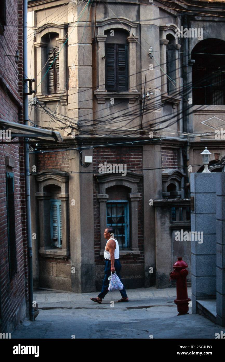 Ein Mann läuft an alten Ziegelgebäuden in Shanghai, China, vorbei und trägt eine Tasche in einem Stadtviertel. Stockfoto