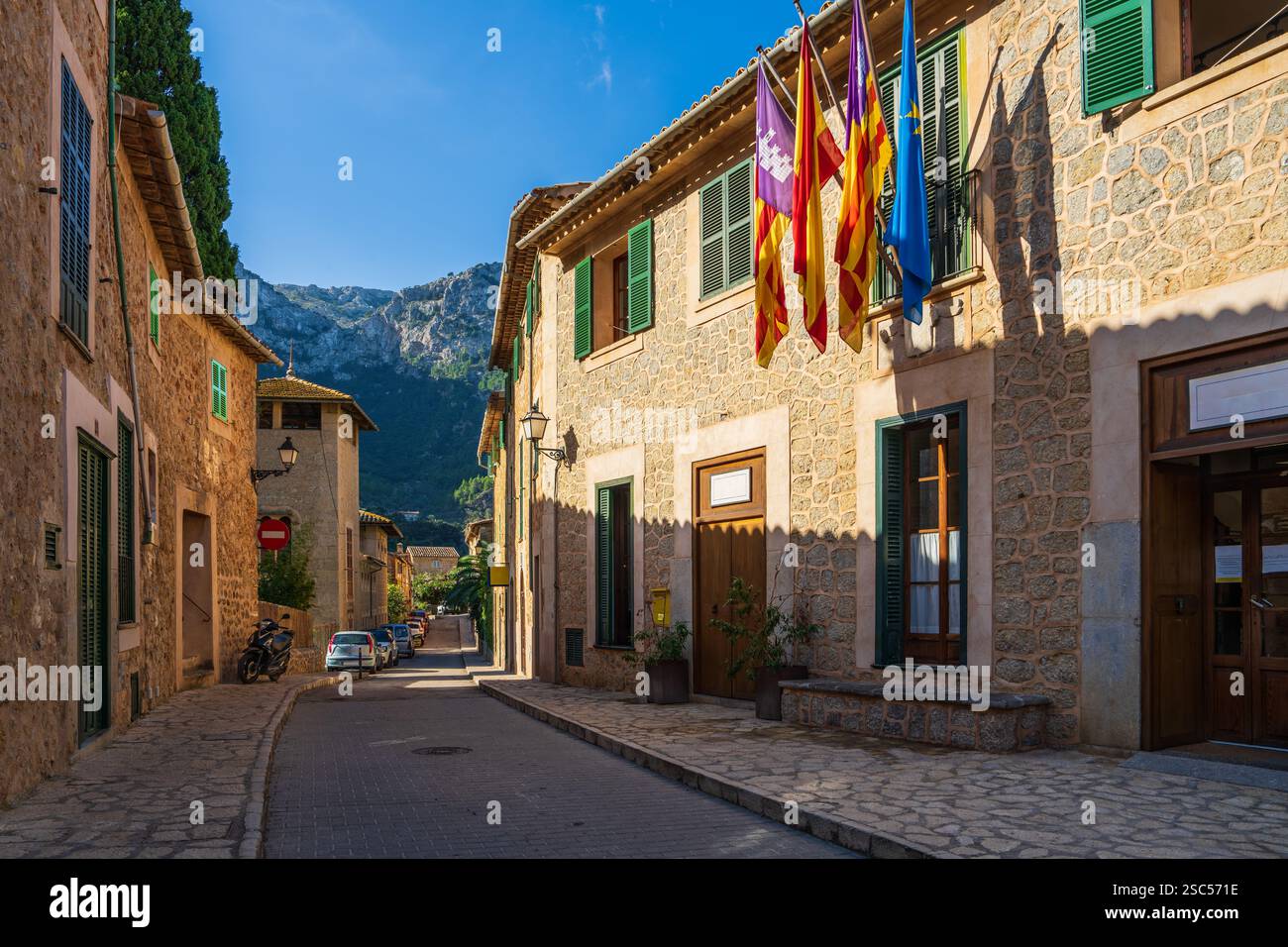 Enge Straße im Dorf Deia, Mallorca, gesäumt von rustikalen Steinhäusern. Fenster mit vielen bunten Fahnen dekoriert. Balearen, Spanien Stockfoto