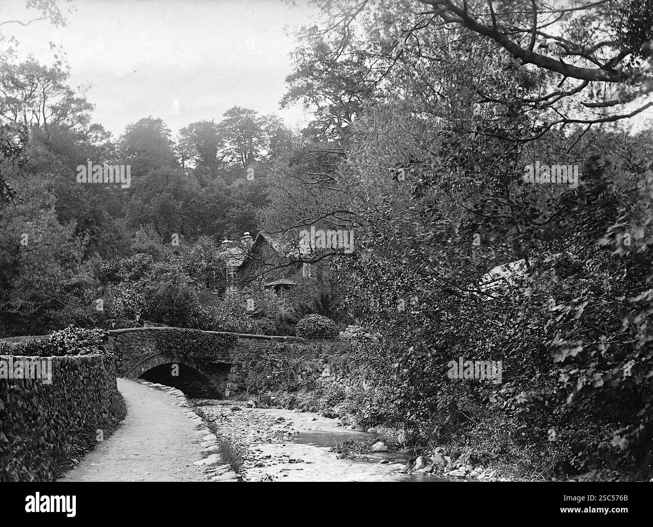 Landschaft mit einem Bach mit einer aus Stein gebauten Bogenbrücke und Mauer und einem Fußweg in Dolgellau, in den Ausläufern von Cadair Idris, Nordwales. 1900, monochrom: Aus einer bedeutenden historischen Sammlung von originalen, nicht zugeschriebenen Albumenfotos aus der späten viktorianischen bis frühen Edwardianischen Zeit: Eine britische Tour einschließlich Staffordshire, Warwickshire und Nordwales. Die Qualität der Originale war variabel und die meisten waren etwa 108 x 165 mm. Stockfoto