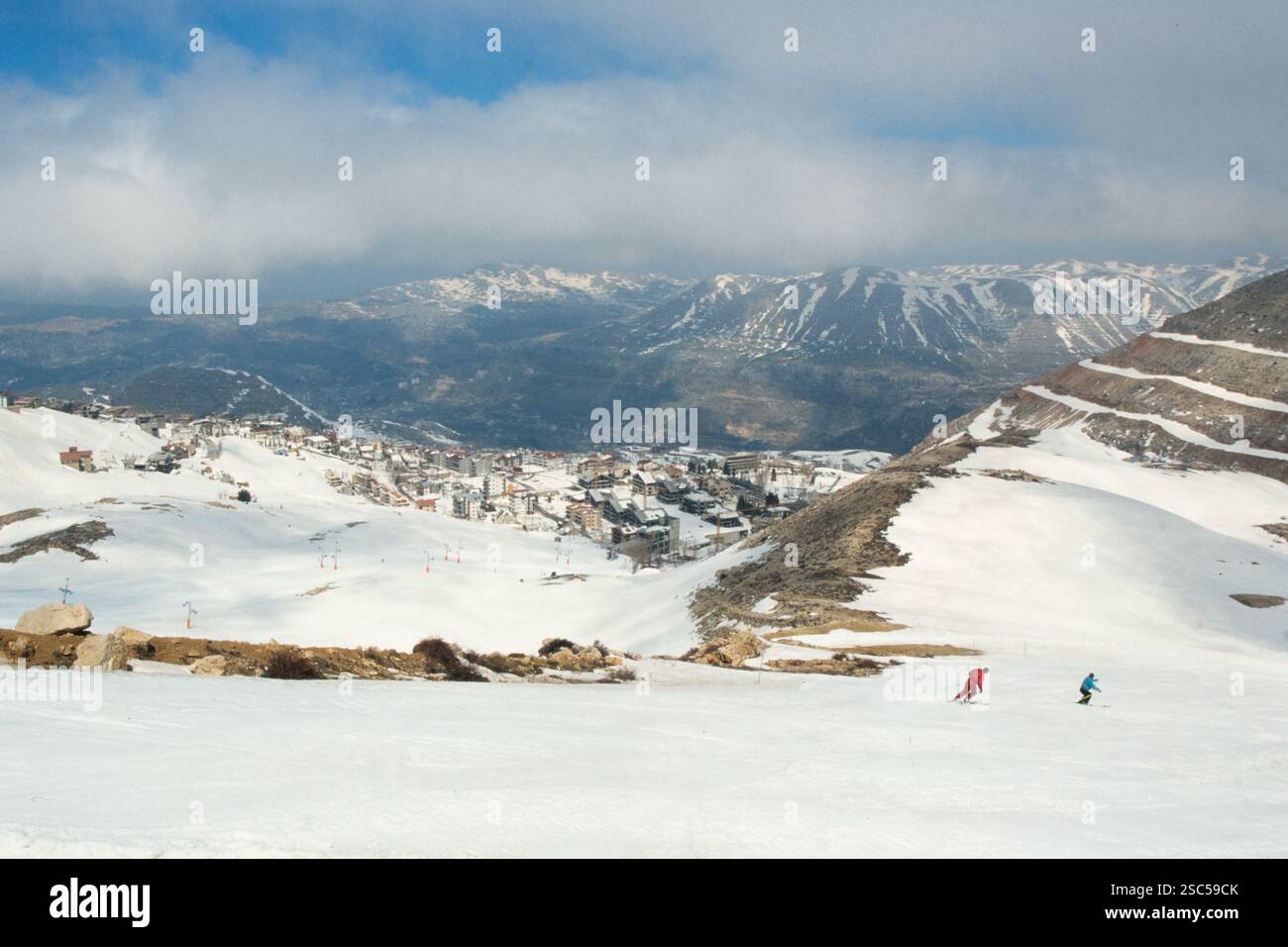 Skifahrer auf verschneiten Pisten im Mzaar Kfardebian, Libanon, mit Bergen und Dorfgebäuden im Hintergrund. Stockfoto