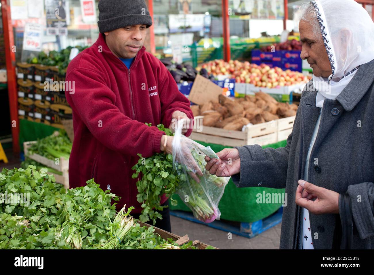 Ein Anbieter verkauft frischen Koriander an einen Kunden auf einem Markt in Birmingham, Großbritannien. Stockfoto