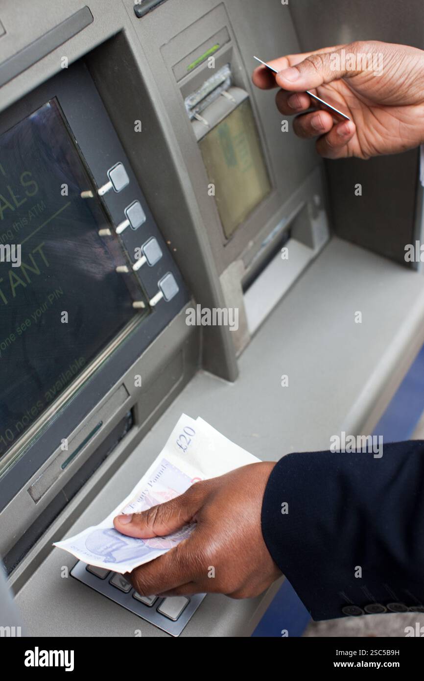 Eine Person hebt mit einer Bankkarte Bargeld von einem Geldautomaten ab und zeigt Geldscheine in Höhe von 20 Pfund an. Stockfoto