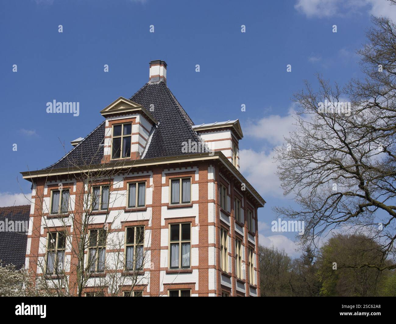 Ein großes Backsteinhaus mit einem dunklen Dach unter einem klaren blauen Himmel, Apeldoorn, Niederlande Stockfoto