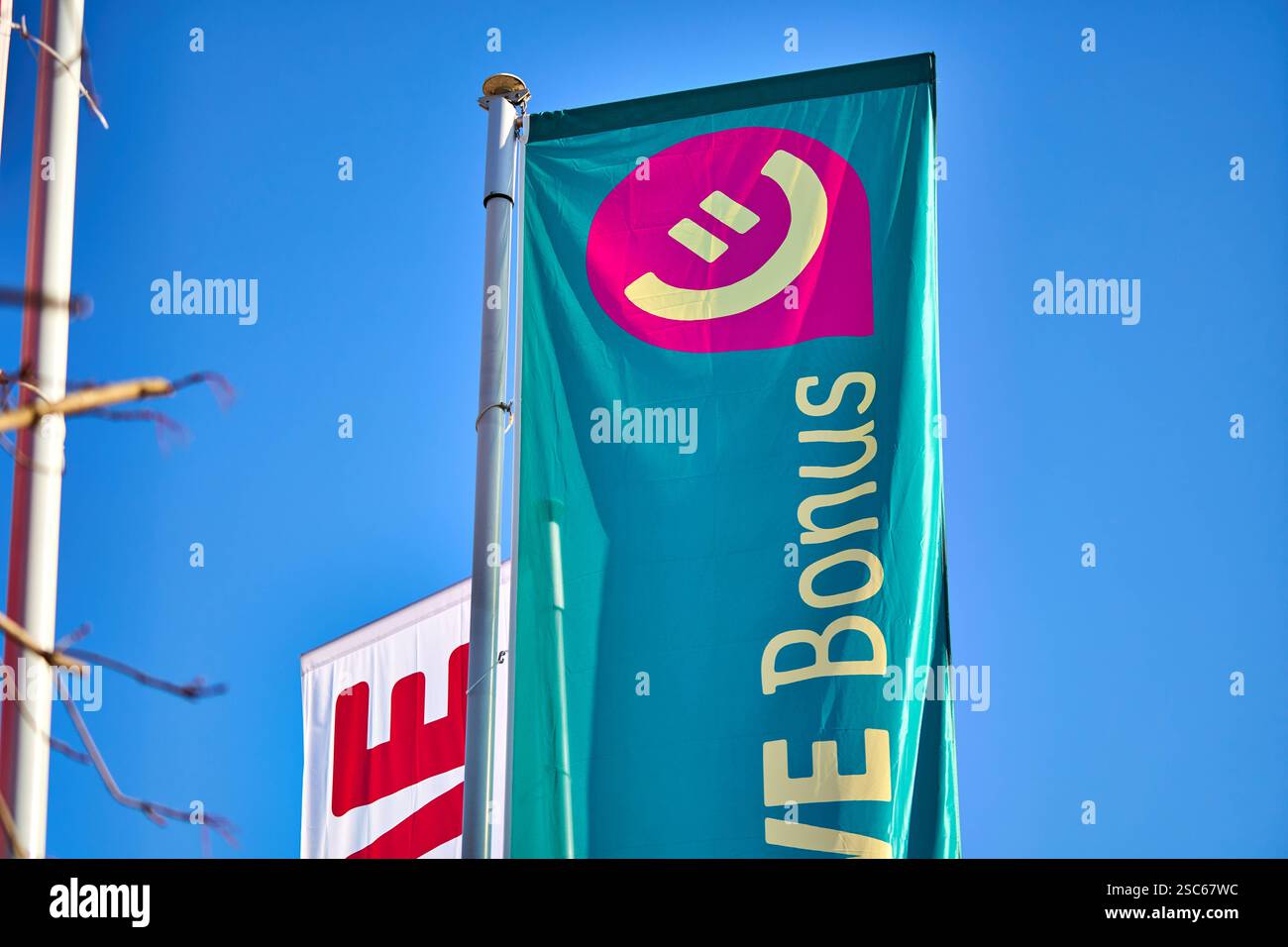 Baden-Württemberg, Stuttgart, Deutschland - 5. Februar 2025: Eine Flagge mit dem Logo des neuen REWE Bonusprogramms weht im Wind vor klarem Himmel. Das Kundenprogramm bietet Rabatte. Sammeln Sie Euro in der REWE App, wenn Sie in REWE Shops einkaufen. *** Eine Fahne mit dem Logo des neuen REWE Bonusprogramme weht im Wind vor klarem Himmel. Das Kundenprogramm bietet Rabatte Sammle Euros in der REWE App beim Einkaufen in REWE-Märkten. Stockfoto