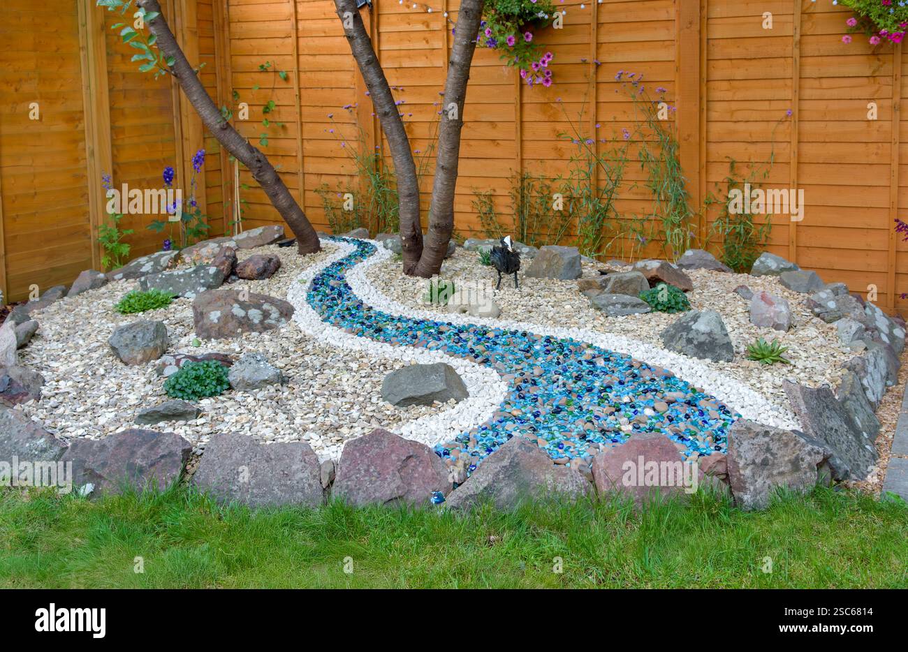 Schönes Haus Garten Rockery Bereich mit Pflanzen, kleinen Felsbrocken, Eisenhut Ornament und Fluss aus Glaskieseln Stockfoto